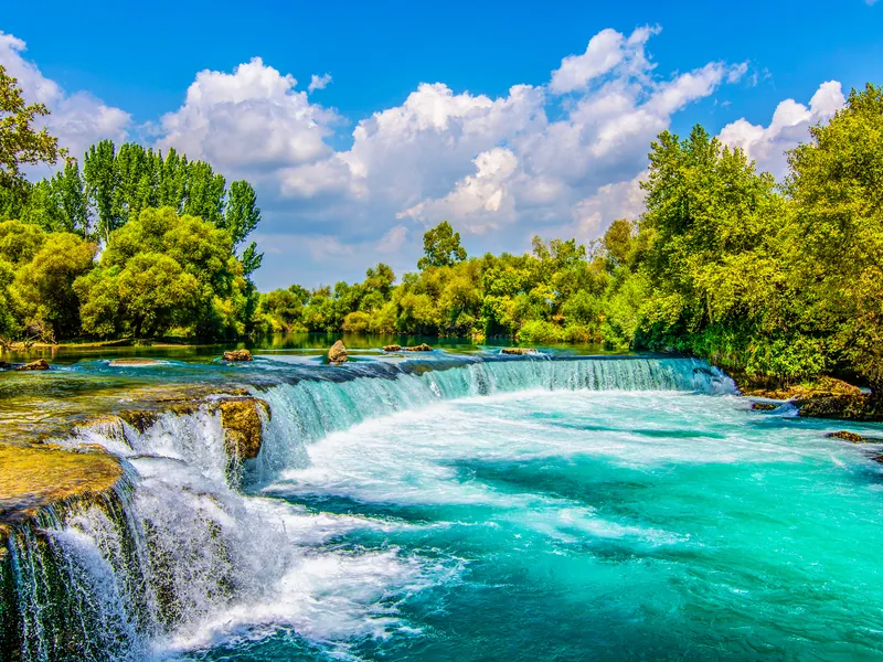 The wide, low Manavgat waterfall with trees along both banks