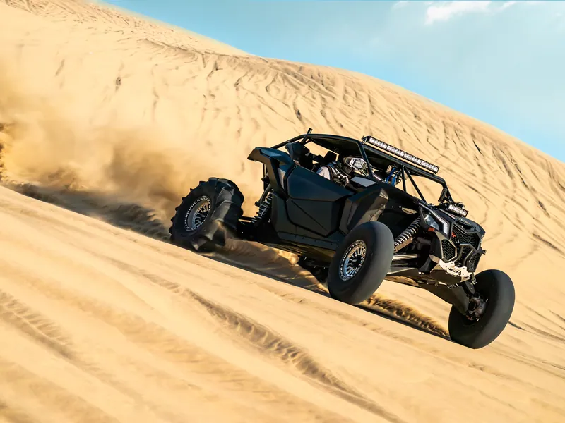 A dune buggy throwing up sand on a desert ridge