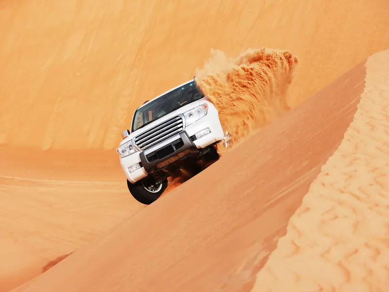 A 4x4 cresting a steep sand dune in the desert