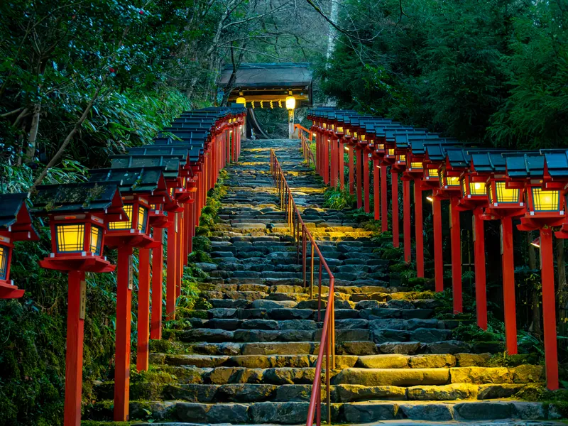 Stone steps lined with red lanterns climbing to a shrine
