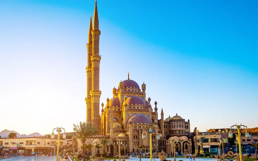 A large sandstone mosque with domes and minarets under a clear blue sky