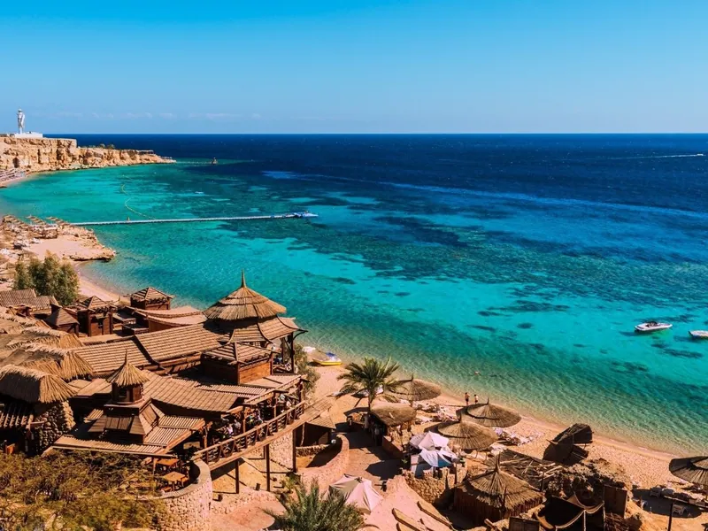 A beach lined with thatched shelters beside deep blue Red Sea water