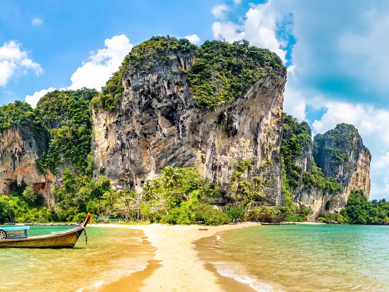 Longtail boats moored off Railay beach beneath a huge limestone cliff