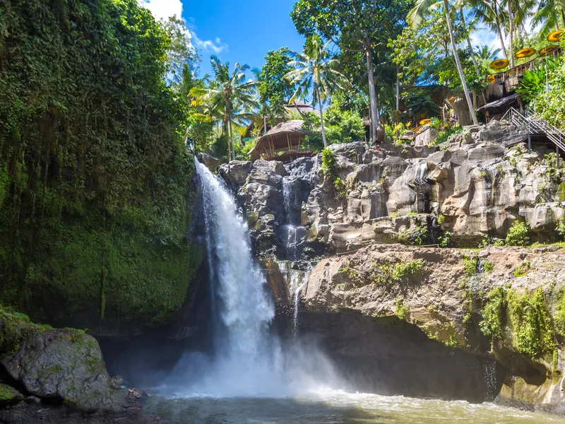 A wide waterfall dropping into a river pool surrounded by jungle