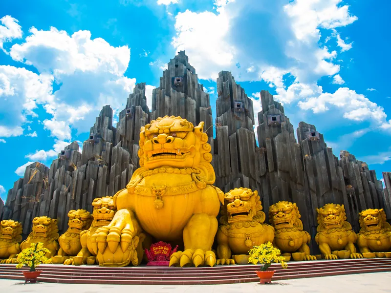 A golden statue group at a mountain temple under a bright sky