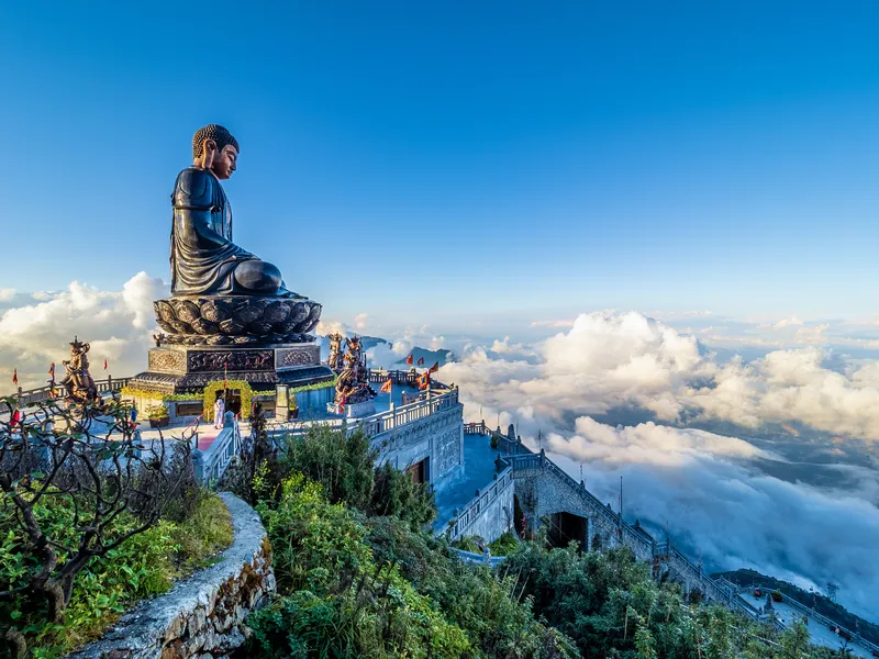 A large seated bronze Buddha on a mountain top above cloud