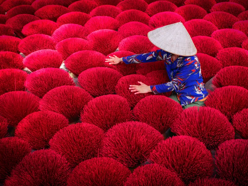 A worker arranging bundles of bright red incense sticks