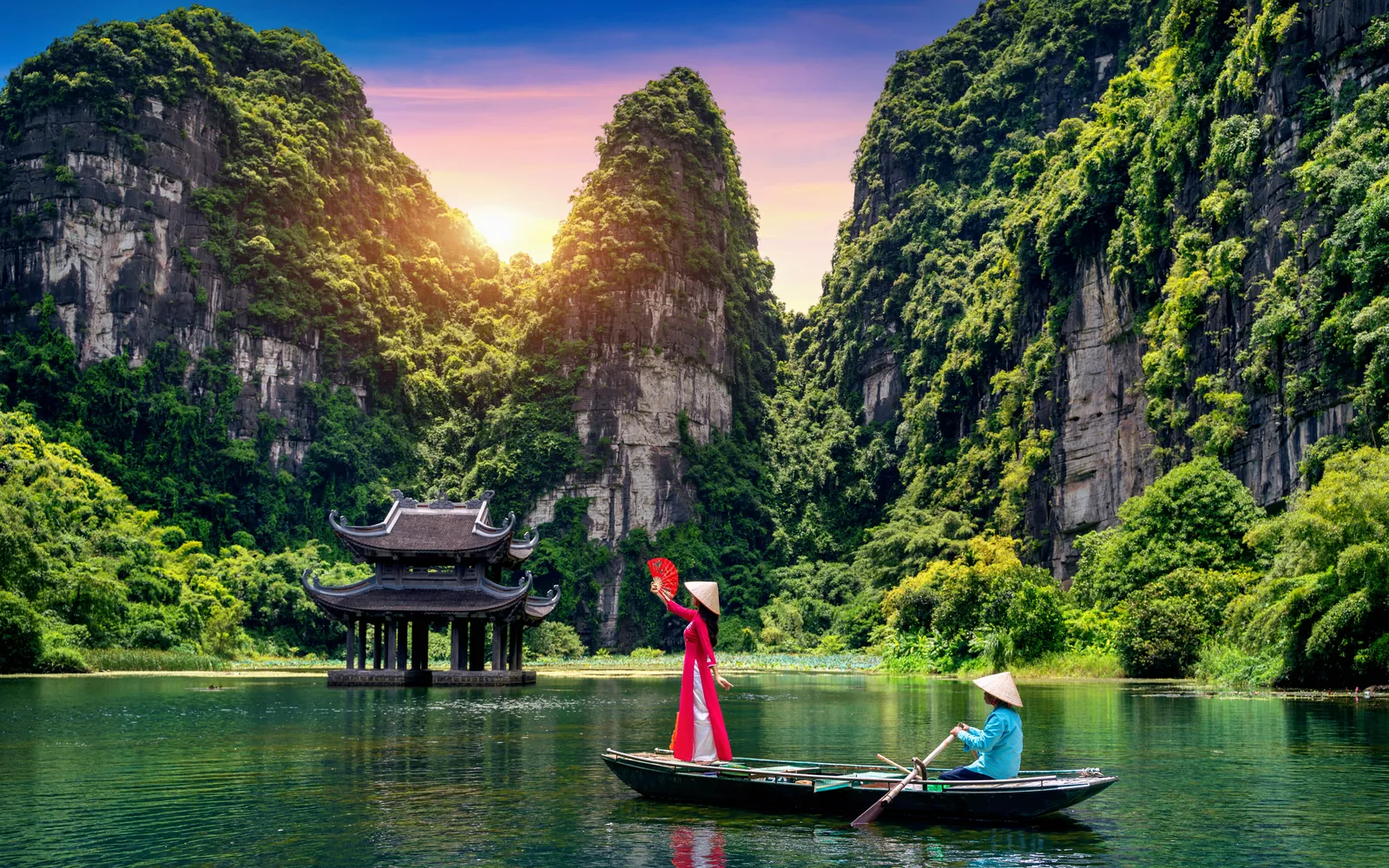 A wooden boat on green water between limestone peaks at Trang An